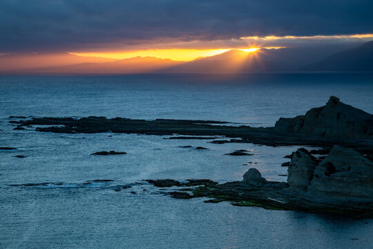 Rugged coastal jagged rocks at sunset with sunburst