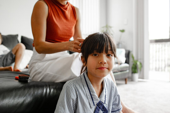 Mother tying the hair of young daughter sitting on the floor