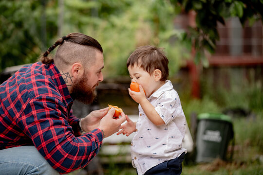 Toddler boy eating half of an orange while dad crouching holding the other half