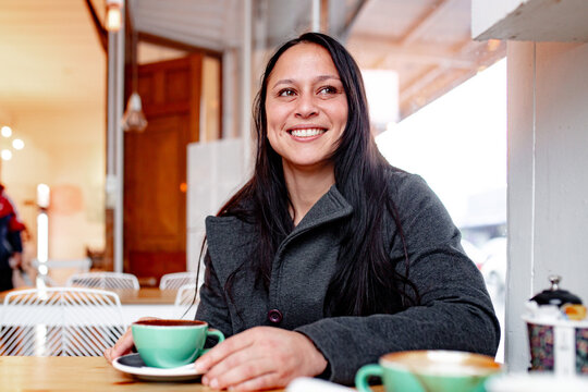 Happy Maori woman sitting at cafe table with a coffee