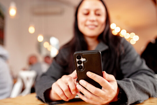Maori woman sitting at cafe table with a coffee holding her phone