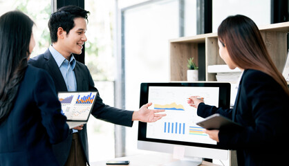 Smiling business team analyzing financial growth charts on computer and digital devices during a collaborative office meeting, focusing on data strategy and professional teamwork.
