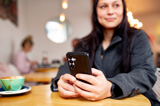 Maori woman sitting at cafe table with a coffee holding her phone