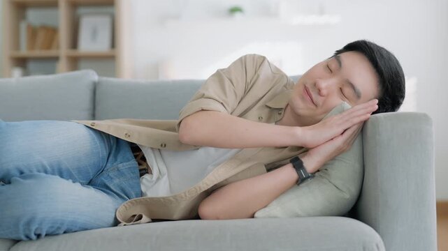 Relaxed young Asian man enjoying rest on comfortable sofa, calm attractive male relaxing on couch