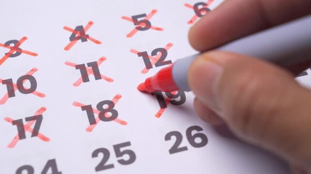 Close up view of a hand crossing out past dates on a paper calendar, marking off days