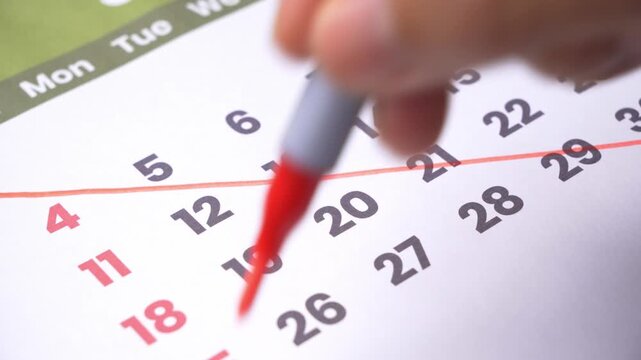 Hand crossing out dates on a calendar page, marking off scheduled events and days