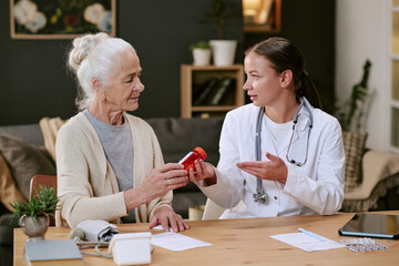 Senior Caucasian woman receiving prescription medication from young adult Caucasian female doctor...