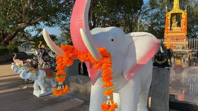 Video of traditional white elephant statues in Thailand decorated with orange flower garlands on tusks, symbolizing Thai religion, spirituality, and cultural heritage at a sacred ceremonial site