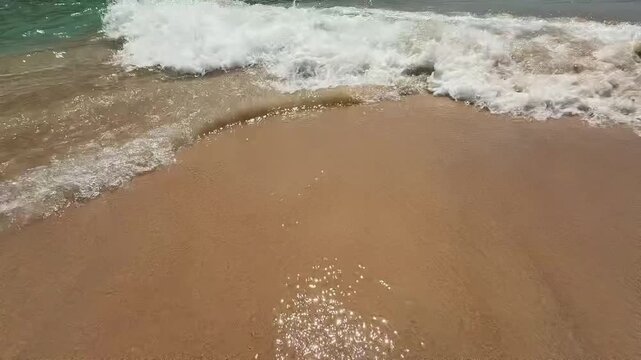 Close up video of bright blue clear waves washing over golden sand on the Andaman Sea coast in southern Phuket, Thailand. Transparent turquoise water and gentle motion highlight tropical shoreline bea