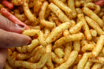 Close up of hand taking spicy cracker stick snack with abundant chili seasoning