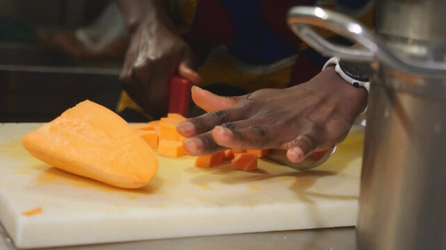 Slow motion close-up shows black woman chef cutting yam Dioscorea spp and sweet potato Ipomoea batatas, known as igname, &ntilde;ame, inhame, batata, kumara, camote and boniato, into concasse cubes