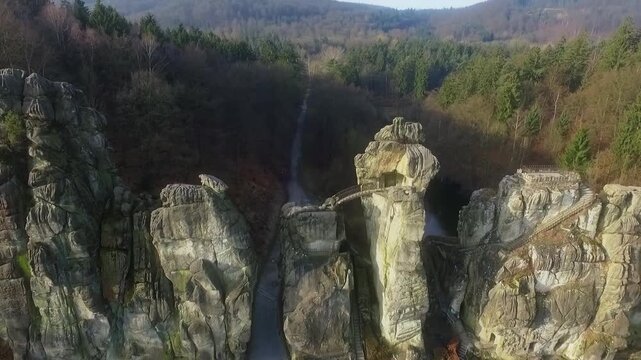 Drone rises and tilts up above Externsteine rocks, revealing forest path and water