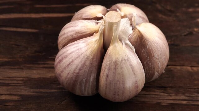 Single garlic bulb slowly rotating on vintage wooden surface. Cinematic studio shot.