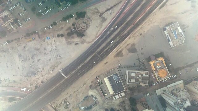 Overhead drone shot through dense fog showing a multi-lane desert highway, sandy lots, parking areas and scattered buildings&mdash;moody atmospheric aerial with low visibility.
