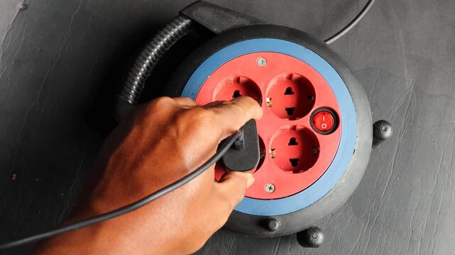Asian man hand plugging an electrical device into a power extension socket at home. Concept of electricity usage, household energy, power connection, electrical safety, and daily technology use.