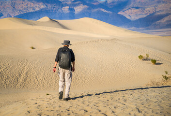 Man walking on rolling sand dunes with mountain range in the distance. Mesquite Flat Sand Dunes....