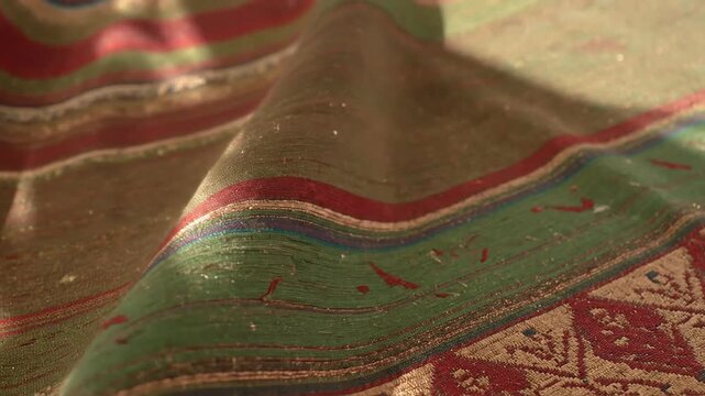 Close-up of richly textured fabric with bold red, green, and gold patterns. A textured masterpiece
