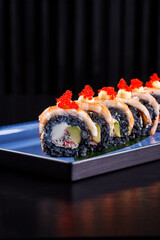 Close-up of premium sushi rolls with black rice, shrimp, avocado, and cream cheese, topped with Japanese mayonnaise and bright red tobiko caviar