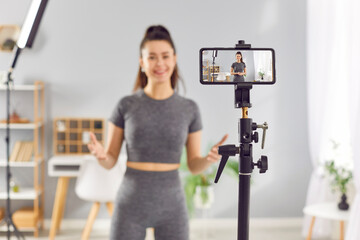 Young sporty woman fitness instructor in sportswear recording video of online training in mobile...