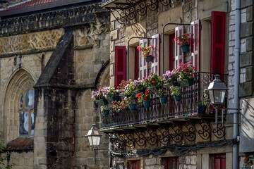 Traditional Balcony with Red Shutters and Flowers in Hondarribia, Spain, Stone Facade