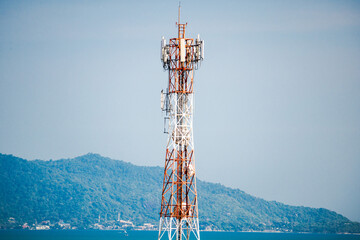Fototapeta premium Telecommunication tower on tropical coastline with blue sea and forested mountains, mobile network infrastructure rising above island landscape and clear sky