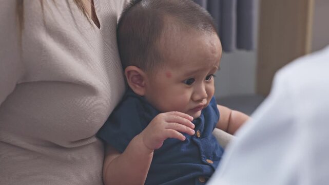Asian female doctor checking infant with red rash on face, showing allergy or skin irritation symptoms during medical examination in premium clinic or private hospital