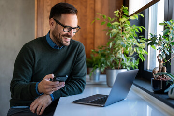Man using smartphone and laptop computer for electronic banking, making reservation, online shopping