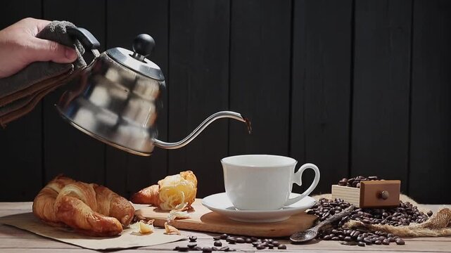 The slow-motion video shows black coffee being poured into a cup. Roasted coffee beans and bread are arranged on the table. The video was filmed with a digital camera and edited by a contributor.