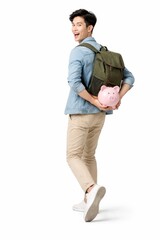 Fototapeta premium Young Asian man with backpack holding piggybank behind back turning toward camera playful savings finance concept isolated on white background