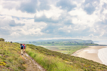 Obraz premium Group of hikers walking on a path in a meadow by the coast