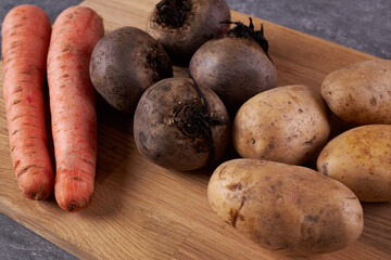 The ingredients for cooking carrots, potatoes and beets are on a wooden cutting board.