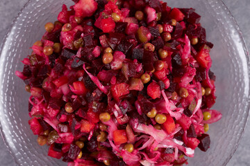 A vinaigrette salad of beets, carrots, potatoes and green peas is on the table in a plate.