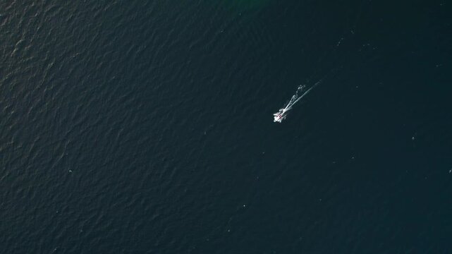 Top down zenithal drone view of Lake Atitlan with a small boat crossing deep blue water creating dynamic contrast and motion.