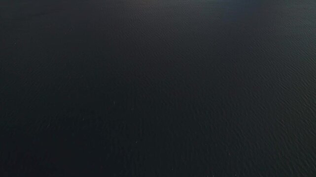 Ascending drone shot rising over calm water framed by volcanic mountains, showing depth and scale of the Lake Atitlan landscape.
