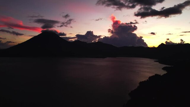 Static aerial view of Lake Atitlan with volcano silhouettes and intense sunset colors filling the sky.