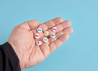 Hand holding mineral supplement pills with chemical symbols on blue background