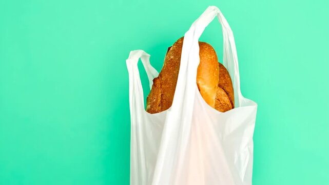 Two loaves of fresh baked bread in a white plastic bag, set against a bright teal background