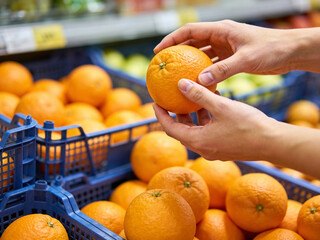 Close-up of hands selecting a ripe orange from a bin overflowing with citrus fruit in a market.