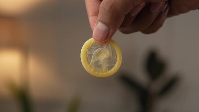 Showing closeup of condom held on fingers.