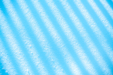Winter snow surface showing intriguing abstract patterns of diagonal shadow stripes, creating a cool blue and white texture background for seasonal or conceptual designs