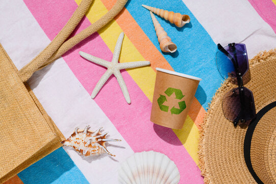 A paper cup with a recycling sign on the beach. A top view of a sustainable tourism concept.