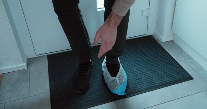 Close-up at the doorway of a professional worker pulling on a blue disposable shoe cover before entering a home. Perfect for home services, hygiene protocols, cleanliness, and customer trust in mainte