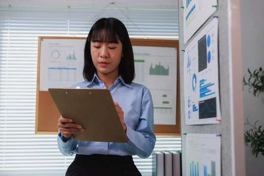 Asian businesswoman analyzing data and writing report in office - Powered by Adobe