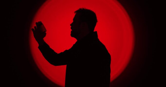 Cinematic side-profile silhouette of a man holding a smartphone against an intense red circular backlight, suggesting compulsive use and digital dependency. Ideal for concepts like screen addiction, s