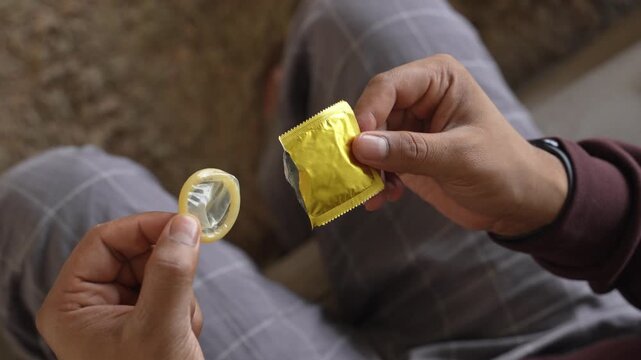 Pulling out a condom from the packet with fingers.