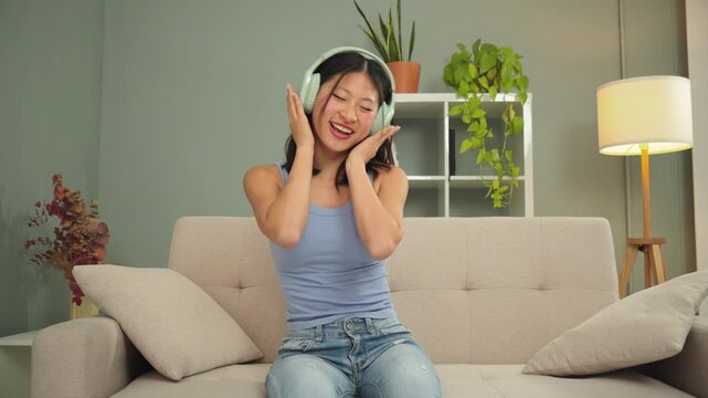 A cheerful young woman is dancing happily at home, enjoying her music through stylish headphones in a cozy living room setting. The vibrant atmosphere adds to her joyful expression and carefree energy