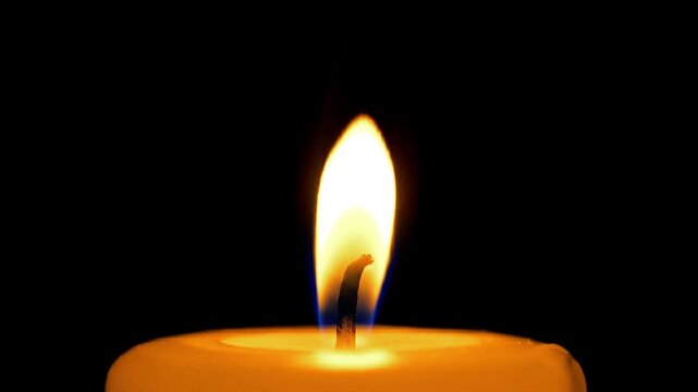 Close-Up of a Single Bright Yellow Candle Flame Against a Dark Black Background
