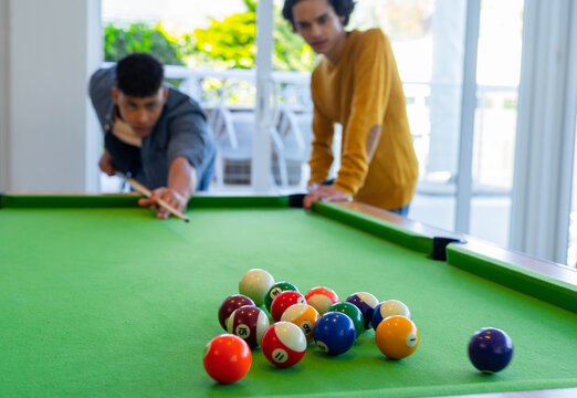 Two men lining up shot on green-felt table near glass doors with cue stick, racked balls