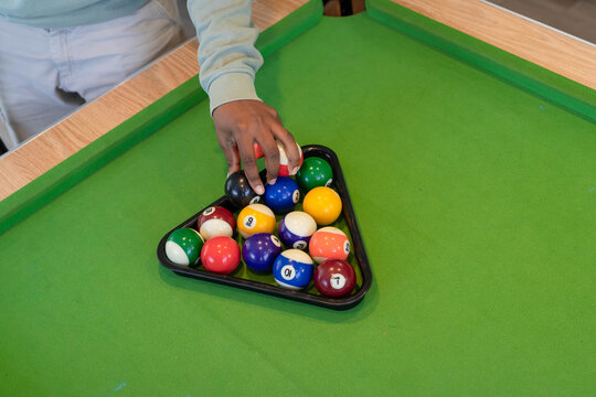 Right hand is placing colorful numbered pool balls in triangular rack on green felt pool table