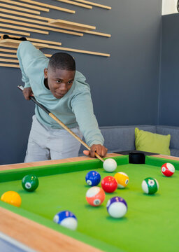 African American man leaning over green-felt pool table, aiming wooden cue at cue ball in lounge